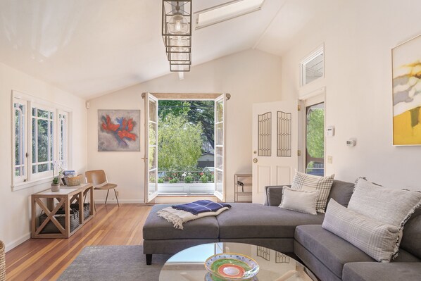 A modern living room with a sectional sofa, a coffee table, and a view of greenery through an open door.