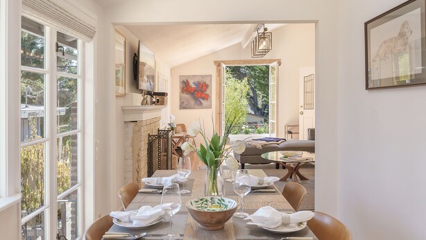 Un coin repas avec une longue table dressée pour six personnes, une cheminée et une vue sur l’extérieur.