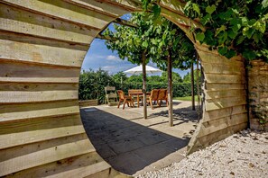 Eine Holz-Pergola mit rundem Durchbruch, eine Steinterrasse und Gartenmöbel.