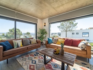 Sala moderna com dois sofás, uma mesa de centro e uma janela ampla com vista para a cidade.