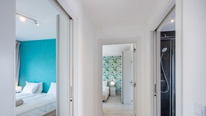 Ein Hotelzimmer mit Bett, einem Badezimmer mit Dusche und einem Flur mit einer Tür zu einem weiteren Zimmer.