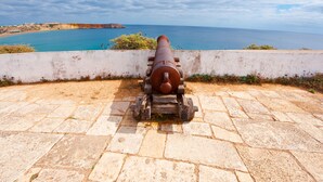 Eine Kanone auf einer Steinterrasse mit Blick auf die Küste und einen klaren Himmel.