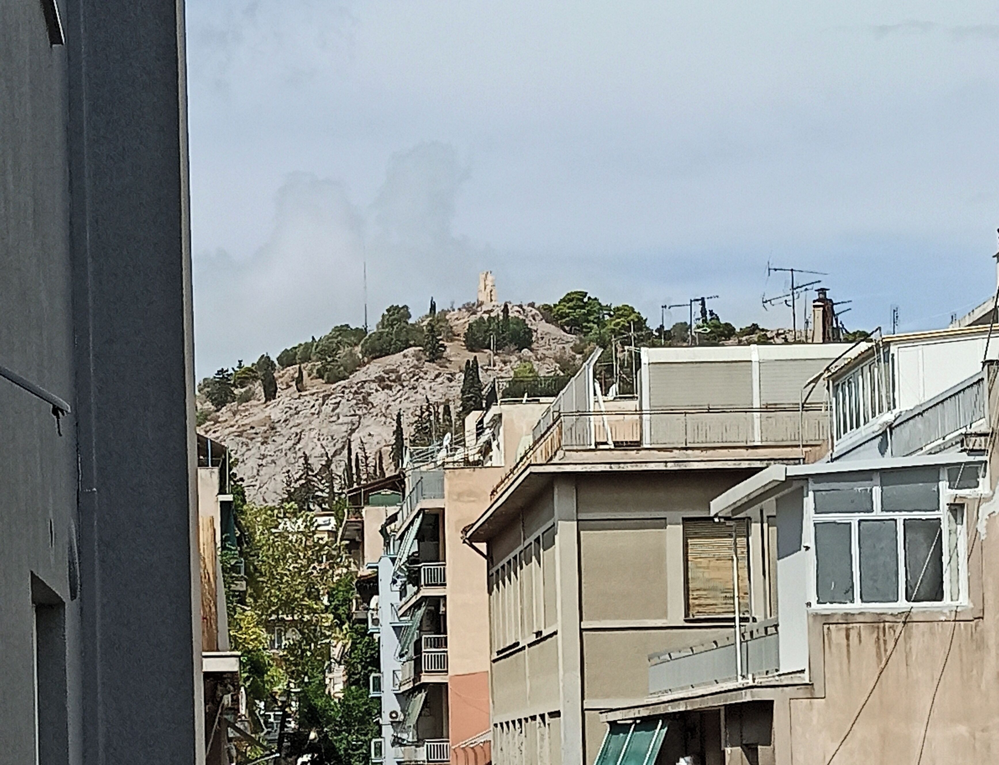 A view of a hillside with a statue on top, surrounded by buildings with balconies and windows.
