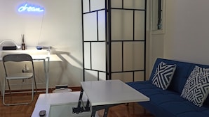 A compact living space with a blue sofa, a white table, and a small desk with a chair. - 2 Bed Flat - Sleeps 5 - Parking - Wifi (Athens)