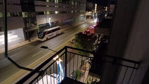 A nighttime view from a balcony overlooking a street with a bus and a building with illuminated windows. - 2 Bed Flat - Sleeps 5 - Parking - Wifi (Athens)