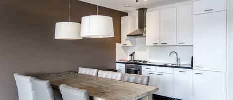 Una cocina moderna con armarios blancos, una mesa de comedor de madera y dos lámparas colgantes.