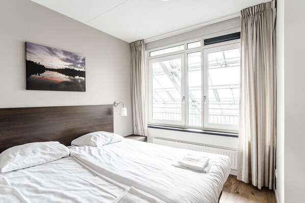 A hotel room with a bed, a nightstand, a lamp, a window with curtains, and a painting on the wall.