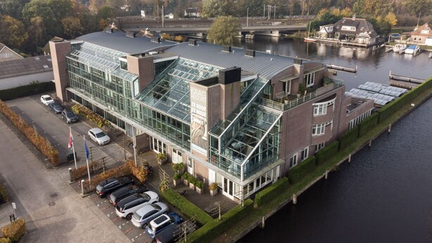 Ein modernes Hotel mit Glasfassade, Parkplatz und Blick auf den Fluss.