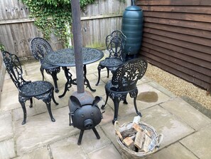Une terrasse avec une table et des chaises en métal, un pot décoratif en forme de cochon et un panier de bois de chauffage.