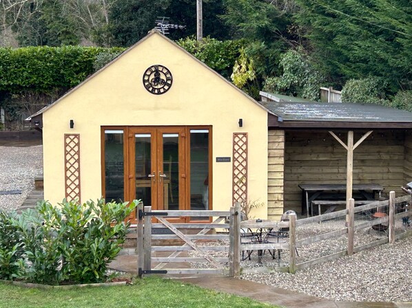 Un petit bâtiment avec une horloge sur la façade, des portes en bois et une clôture en bois qui entoure le terrain.