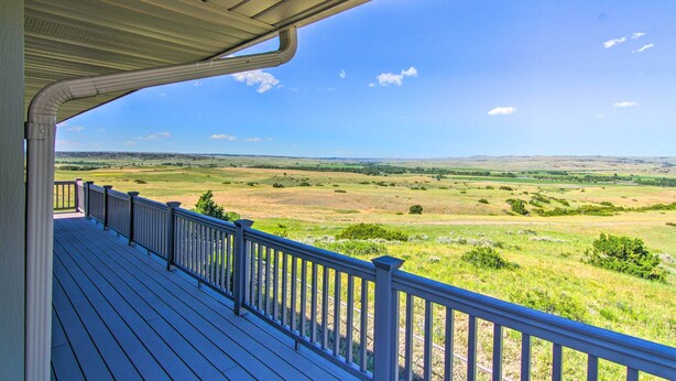Um deck de madeira com guarda-corpo, com vista para uma paisagem gramada.