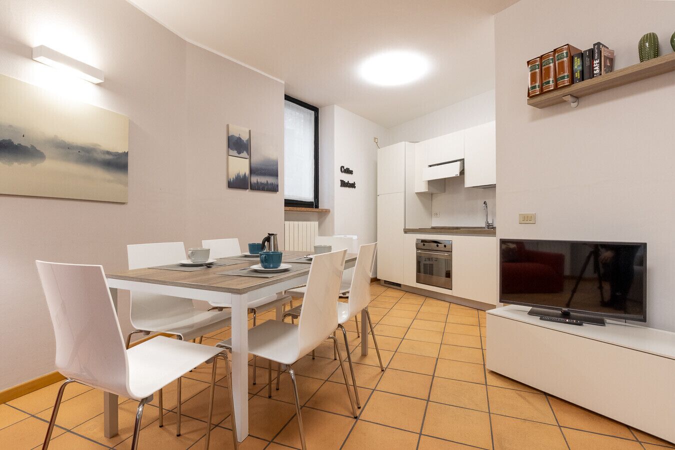 A modern kitchen with white cabinetry, a built-in oven, and a TV.