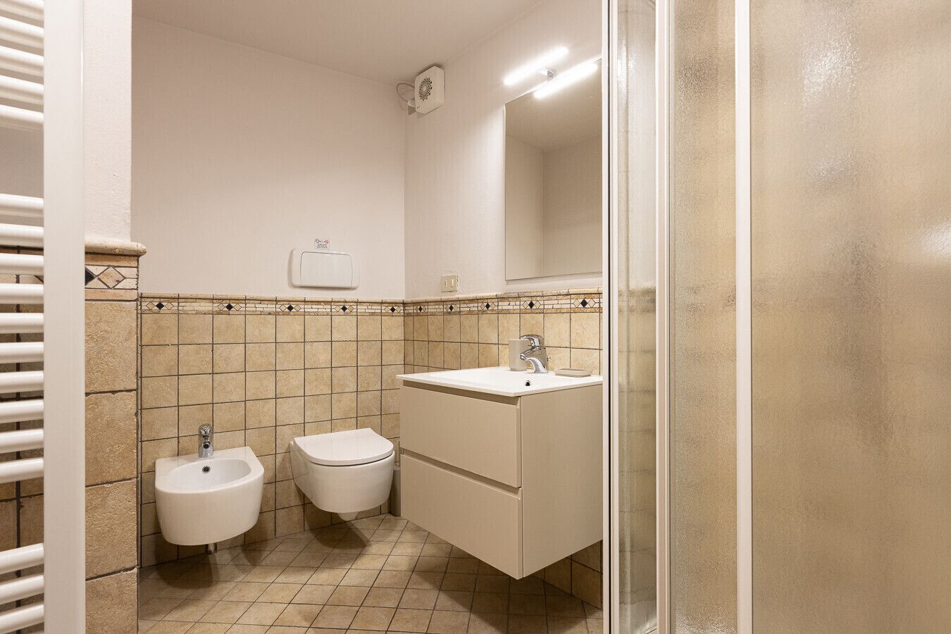 Une salle de bain comprenant des toilettes, un bidet et un lavabo, avec des murs carrelés et un miroir au-dessus du lavabo.