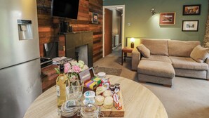 Ein Wohnzimmer mit Kamin, einer Couch, einem an einer Holzwand montierten Fernseher und einem Tisch mit Snacks.