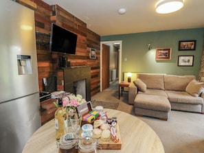 A living room with a fireplace, a sofa, a TV mounted on a wooden wall, and a table with snacks. - Puidrac Cottage (Lochearnhead)