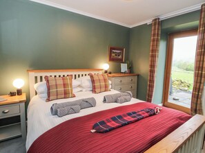A bedroom with a bed, bedside tables, a nightstand, a dresser, a window with curtains, and a view of the outdoors.