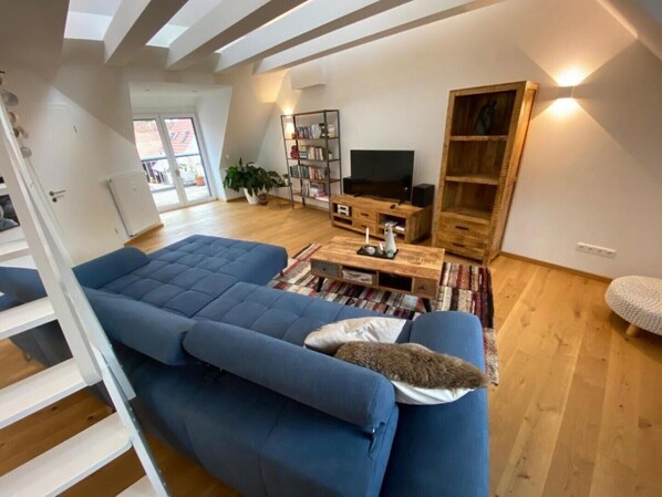Un salon moderne avec un canapé bleu, un plancher en bois, un téléviseur, des étagères et un escalier.
