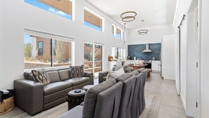 A spacious living area with a grey sofa, a dining table, and a kitchen in the background. - Contemporary Compound By Homestead Modern (Joshua Tree)