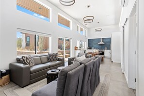 A spacious living area with a grey sofa, a dining table, and a kitchen in the background. - Contemporary Compound By Homestead Modern (Joshua Tree)