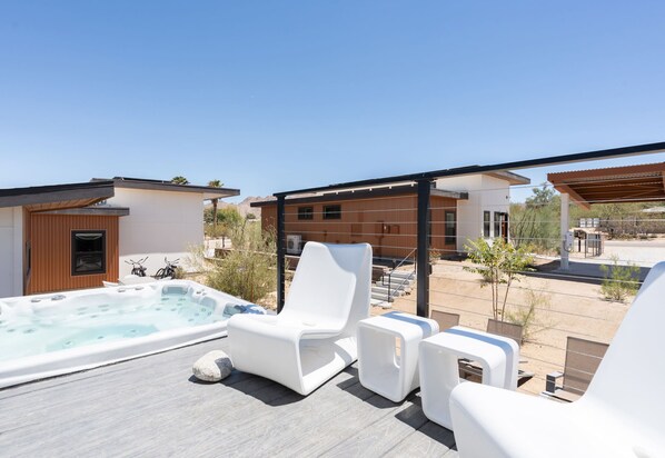 Une terrasse sur le toit avec un jacuzzi, des chaises longues blanches et une pergola en bois.