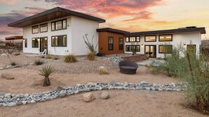A modern two-story house with a patio area, surrounded by desert landscaping. - Contemporary Compound By Homestead Modern (Joshua Tree)