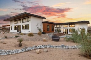 A modern two-story house with a patio area, surrounded by desert landscaping. - Contemporary Compound By Homestead Modern (Joshua Tree)