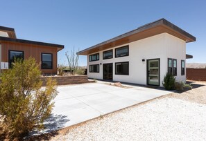 Una casa moderna de dos pisos con un amplio camino de entrada, una terraza de madera y un pequeño jardín.