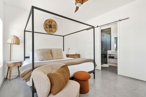 Une chambre moderne avec un lit à baldaquin, un élément de décoration circulaire au mur, une table de chevet, une lampe et une vue sur la salle de bain.