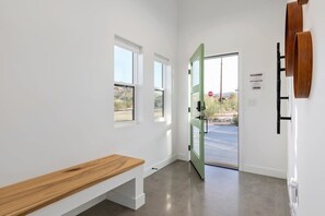 A hallway with a bench, a green door, and windows with a view of the outside. - Contemporary Compound By Homestead Modern (Joshua Tree)
