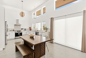 A modern kitchen with a large island, white cabinetry, and a large sliding glass door leading to a patio. - Contemporary Compound By Homestead Modern (Joshua Tree)