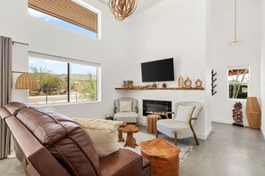 Un salon spacieux avec un canapé en cuir, une cheminée, un téléviseur à écran plat et une grande fenêtre donnant sur l’extérieur.