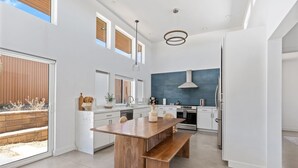 A modern kitchen with a wooden island, white cabinetry, and a large window. - Contemporary Compound By Homestead Modern (Joshua Tree)