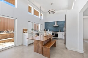 A modern kitchen with a wooden island, white cabinetry, and a large window. - Contemporary Compound By Homestead Modern (Joshua Tree)