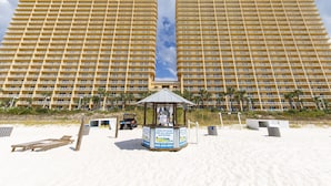 Un grand hôtel avec de nombreux étages et des balcons, une zone de plage avec des transats, et un panneau indiquant les activités proposées sur la plage.