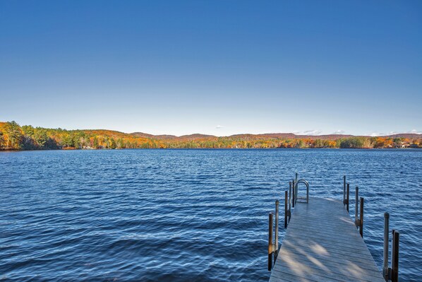 A wooden dock extending into a calm lake with autumn-colored trees in the background. - Hideaway at Highland Lake (Andover)