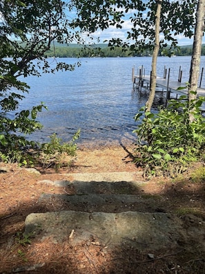 A lakeside view with a dock extending into the water, surrounded by trees and vegetation. - Hideaway at Highland Lake (Andover)