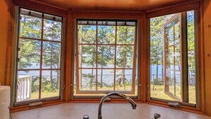 A room with a large bay window overlooking a lake, a built-in sink, and a wooden ceiling. - Hideaway at Highland Lake (Andover)