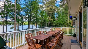 A wooden deck with a table and chairs, overlooking a lake with trees. - Hideaway at Highland Lake (Andover)