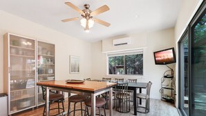 Une cuisine moderne avec une table en bois et des tabourets de bar, un ventilateur de plafond et une grande fenêtre donnant sur la forêt.