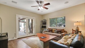 Un salon avec un ventilateur de plafond, un canapé, une table basse et une fenêtre donnant sur des arbres.