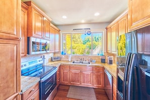 A kitchen with wooden cabinets, a built-in oven, a sink, and a window with a view of trees.
