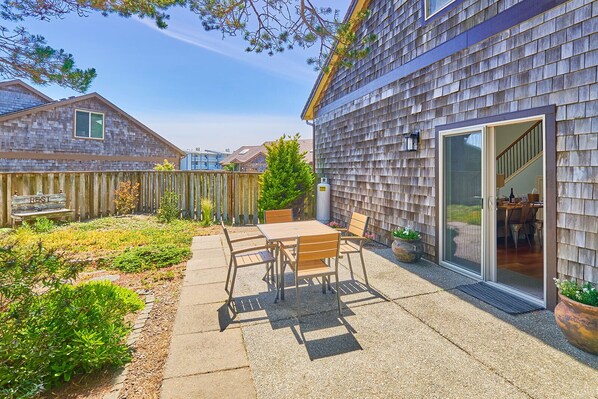 A patio with a table and chairs, a wooden fence, and a house with a sliding glass door.