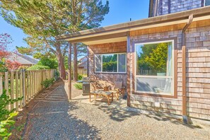 Une terrasse couverte, aménagée avec du mobilier d’extérieur, un barbecue et un chemin de gravier menant à une clôture en bois.