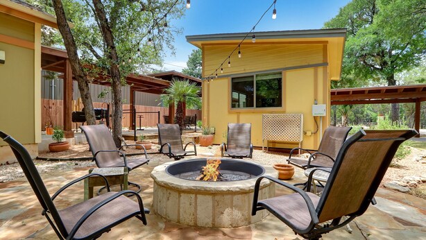 A patio area with a circular fire pit surrounded by chairs, a yellow building, and trees. - Three Sisters- Casita 1   I Pet Friendly couples retreat in Wimberley (Wimberley)