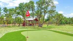 A golf course with a putting green, a flag, and a small pavilion surrounded by trees. - Three Sisters- Casita 1   I Pet Friendly couples retreat in Wimberley (Wimberley)