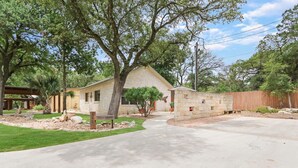 A two-story house with a stone facade, a front yard with a pathway, and a wooden fence. - Three Sisters- Casita 1   I Pet Friendly couples retreat in Wimberley (Wimberley)