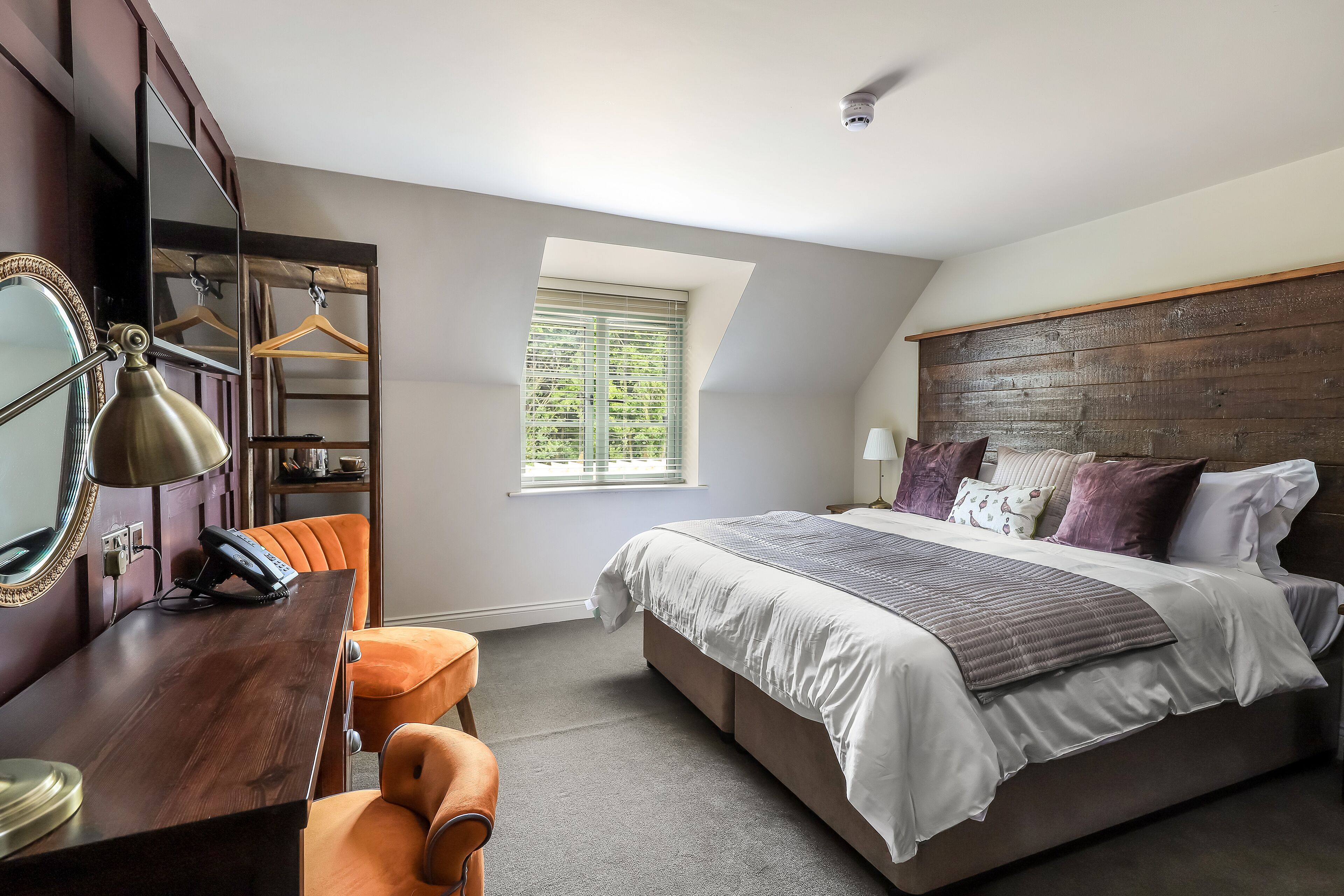 A bedroom with a large bed, a desk, a chair, a wardrobe, and a window with blinds.