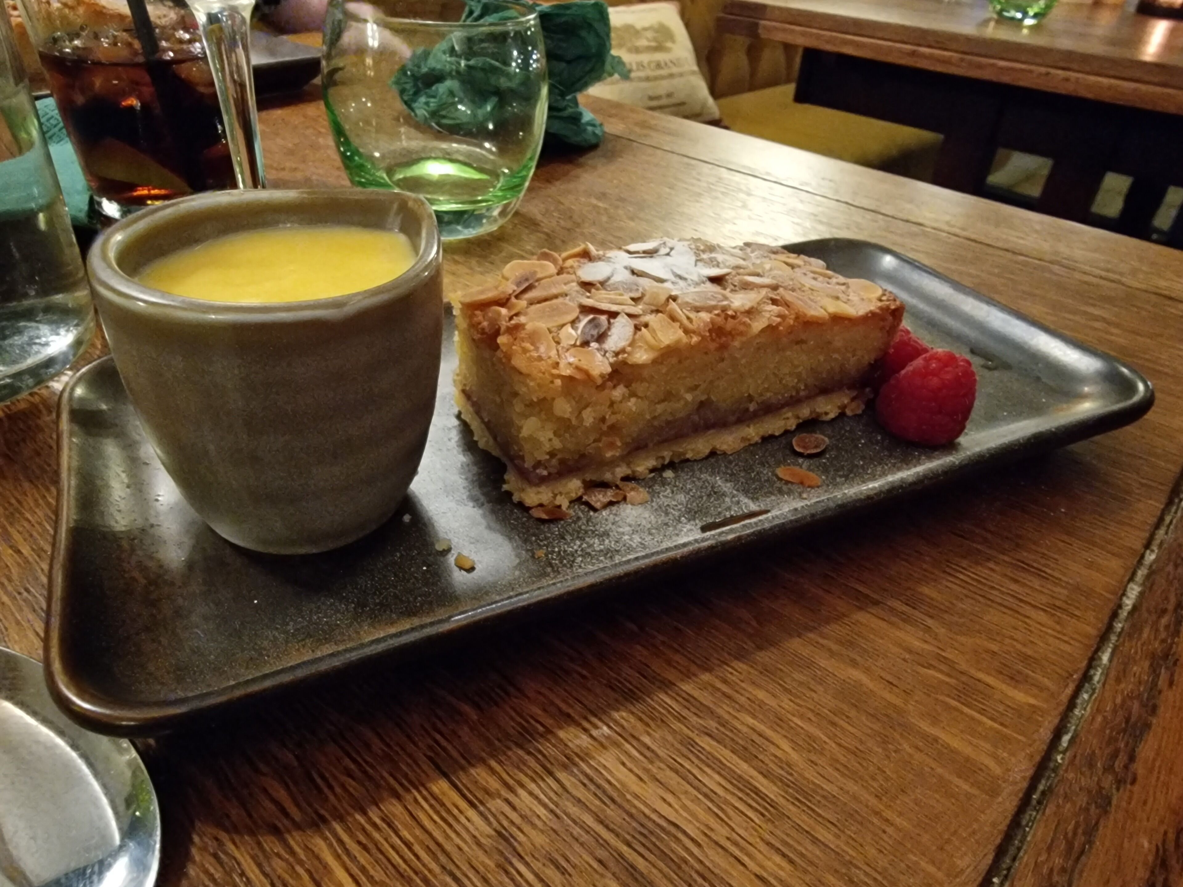 Una bandeja de postres con una porción de pastel y un tazón pequeño de salsa sobre una mesa de madera.