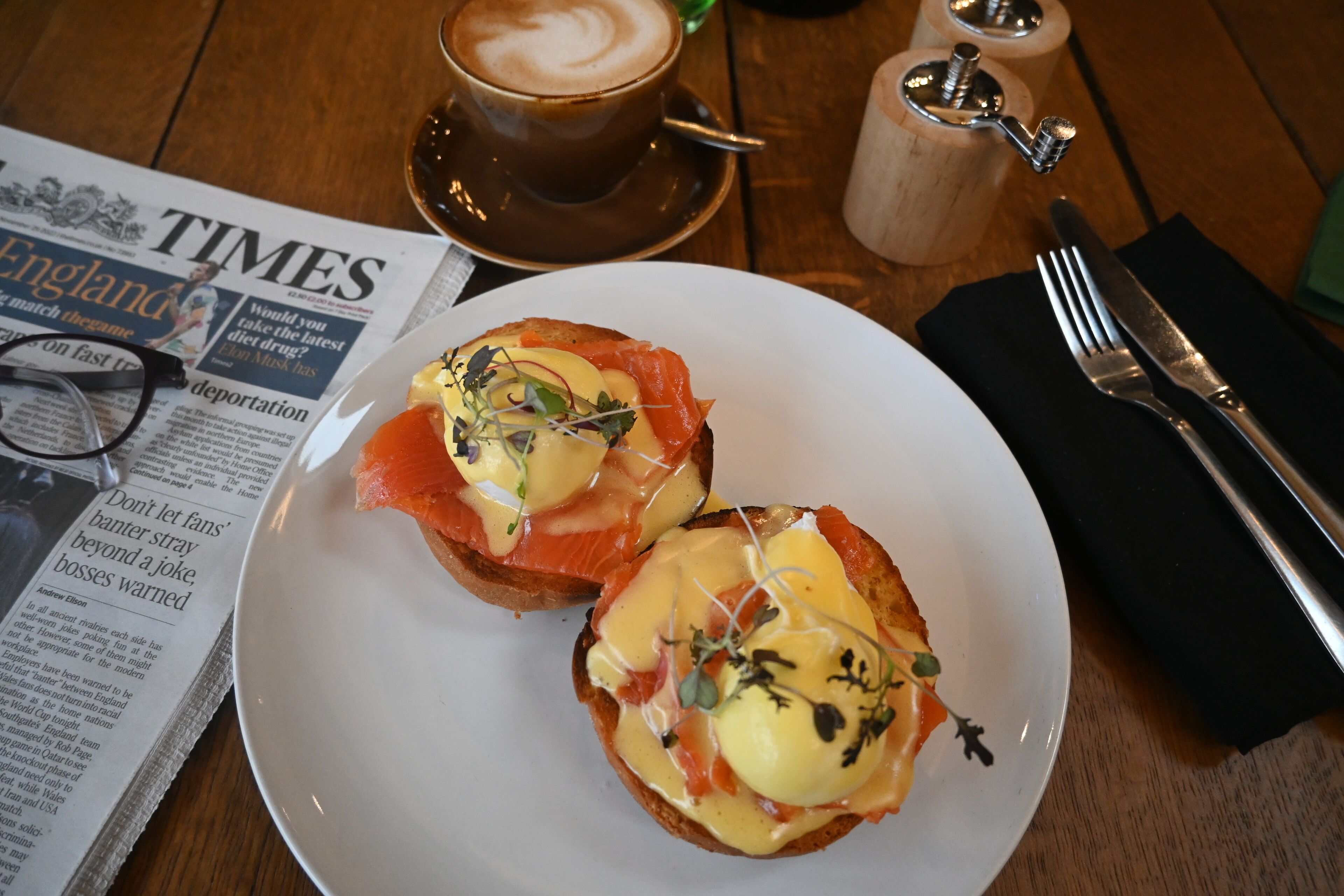 Una mesa con un periódico, una taza de café y dos platos de comida.