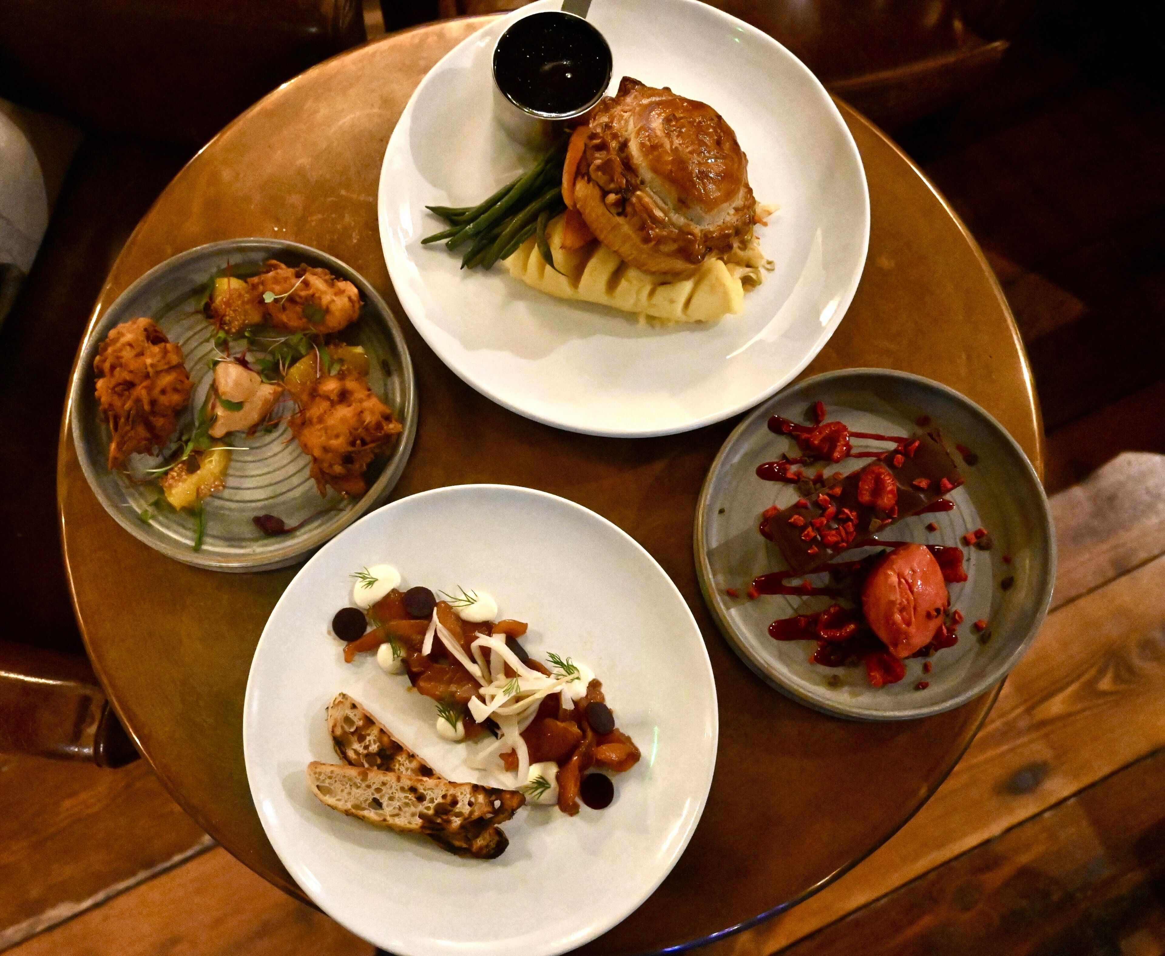 A table with four plates of food, including a burger, salad, and other dishes.